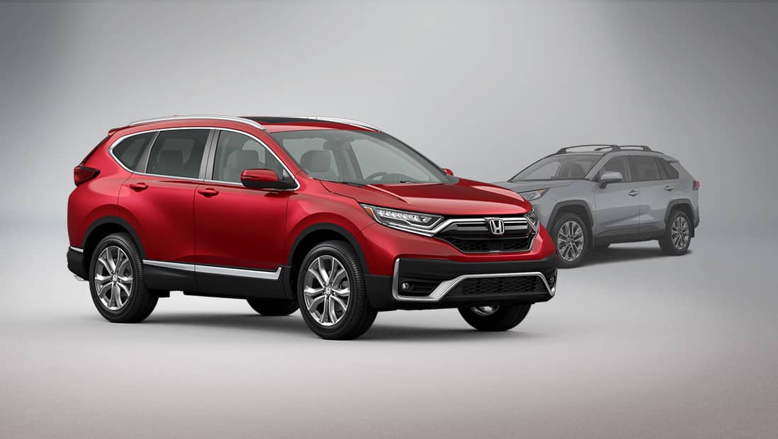 Vista frontal del lado del pasajero de la Honda CR-V Touring 2020, en Deep Scarlet Pearl, estacionada en un estudio junto a una Toyota RAV4.