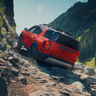 2027 Honda Passport TrailSport Elite in Radiant Red Metallic II back climbing a steep rocky mountain trail (Mid-Size SUV).
